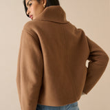 A woman wearing a cropped camel brown wool-blend jacket with a high folded collar, shown from a three-quarters back view against a solid beige studio background.
