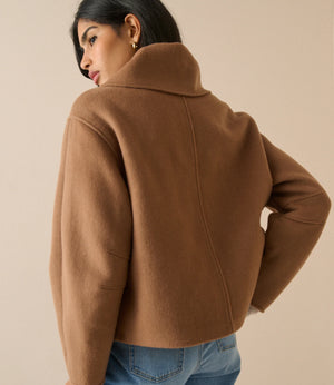 A woman wearing a cropped camel brown wool-blend jacket with a high folded collar, shown from a three-quarters back view against a solid beige studio background.