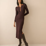 A woman modeling a long-sleeve, knee-length knit dress in deep plum brown with a contrasting tan collar and button placket, paired with dark brown knee-high boots, set against a plain beige studio background.