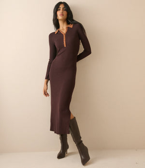 A woman modeling a long-sleeve, knee-length knit dress in deep plum brown with a contrasting tan collar and button placket, paired with dark brown knee-high boots, set against a plain beige studio background.