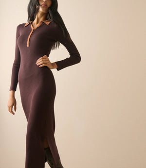 A woman modeling a long-sleeve, bodycon knit midi dress in a deep plum-brown color with contrasting tan collar and placket trim, paired with dark brown boots against a plain beige studio background.