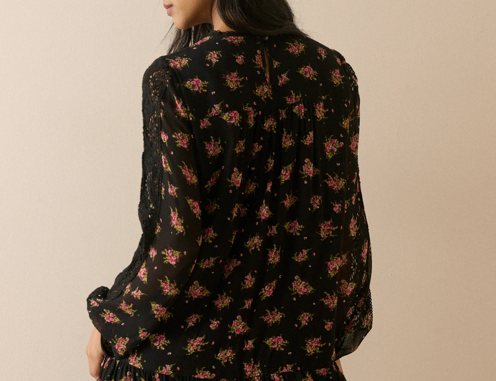 A woman wearing a black long-sleeve mini dress with a pink and yellow floral print, shown from the back against a solid beige background.