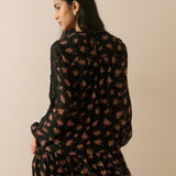 A woman wearing a black long-sleeve mini dress with a pink and yellow floral print, shown from the back against a solid beige background.