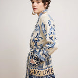 A model wearing a cream-colored knit cardigan with blue and navy patterns, featuring fringe details and a printed design with the words 'MAGNIFICATION LOVE'.