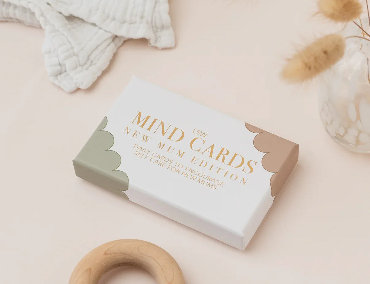 Box of 'New Mum Edition' cards on a light surface with a wooden ring and fabric.