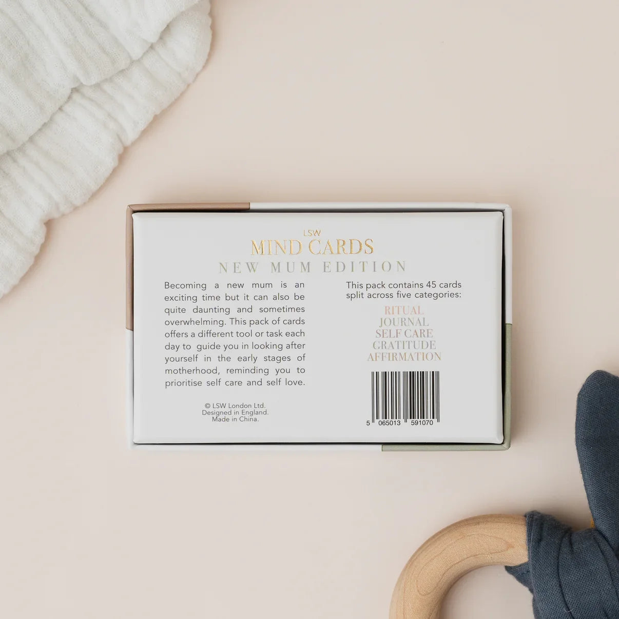 Packaging of 'New Mum Edition' mind cards on a beige surface with a baby's bootie and blanket.
