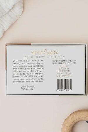 Packaging of 'New Mum Edition' mind cards on a beige surface with a baby's bootie and blanket.