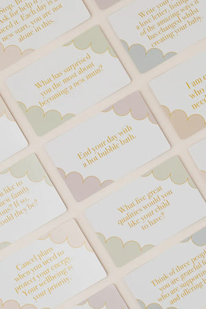 A close-up of multiple cream-colored cards with scalloped edges, printed with soft pastel text and gold lettering, arranged diagonally on a light beige background.