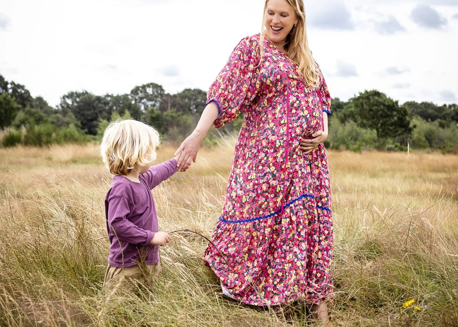 Woman and child holding hands in a field with a cloudy sky.