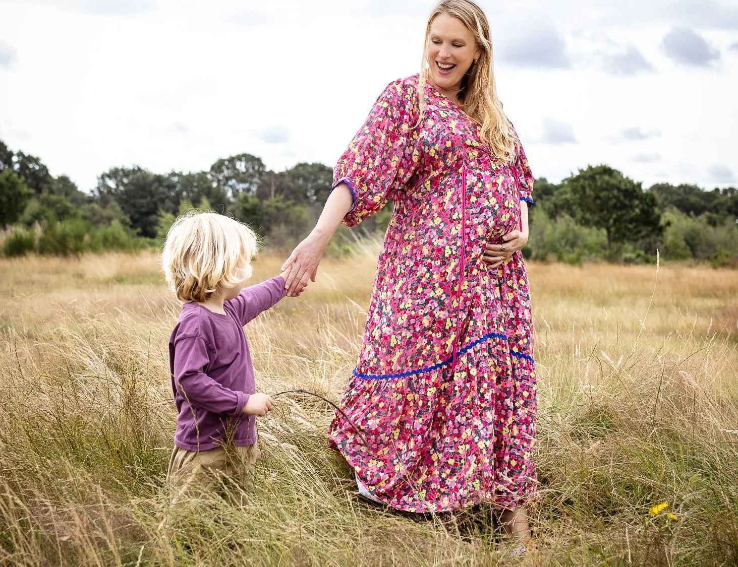 Woman and child holding hands in a field with a cloudy sky.
