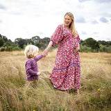 Woman and child holding hands in a field with a cloudy sky.