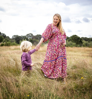 Woman and child holding hands in a field with a cloudy sky.