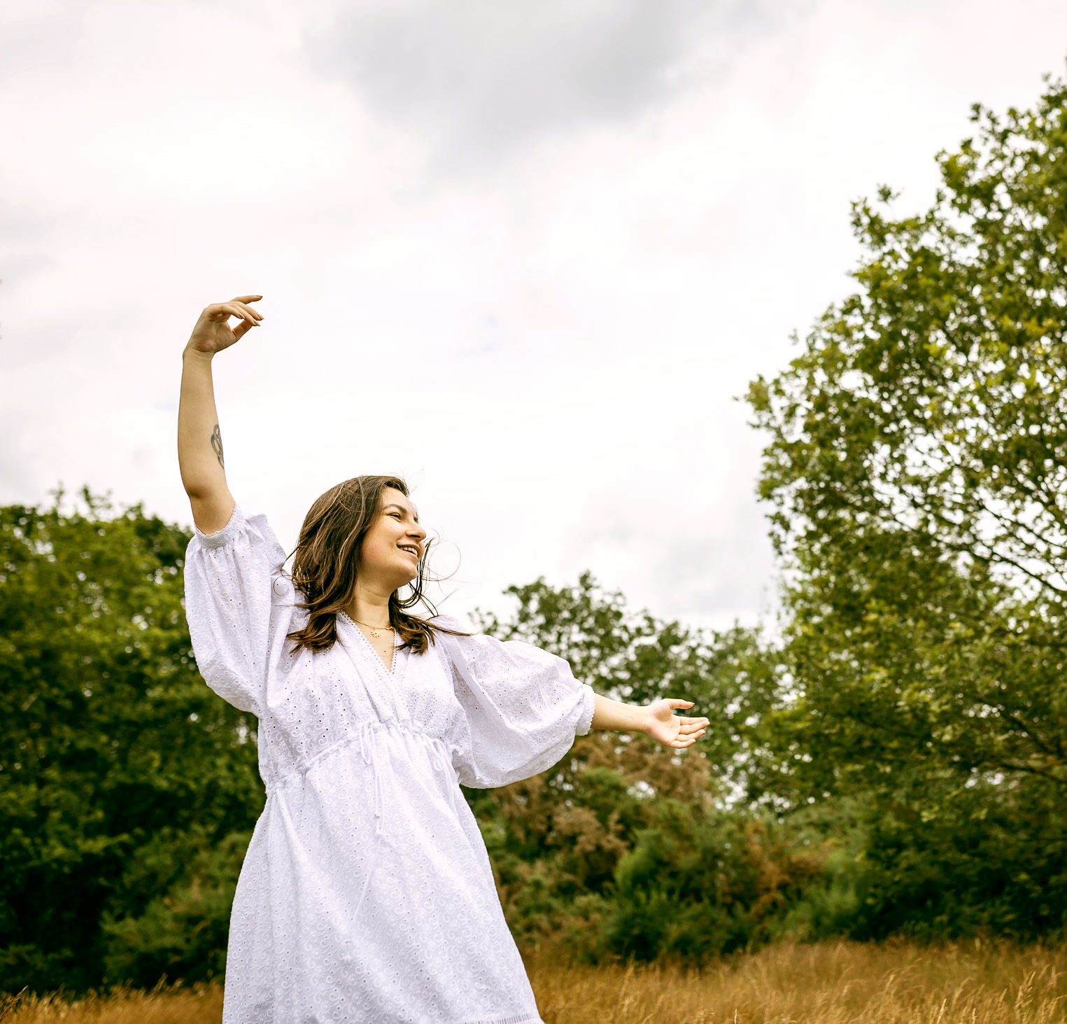 Woman in a white dress standing in a field with trees in the background