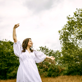 Woman in a white dress standing in a field with trees in the background