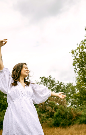 Woman in a white dress standing in a field with trees in the background