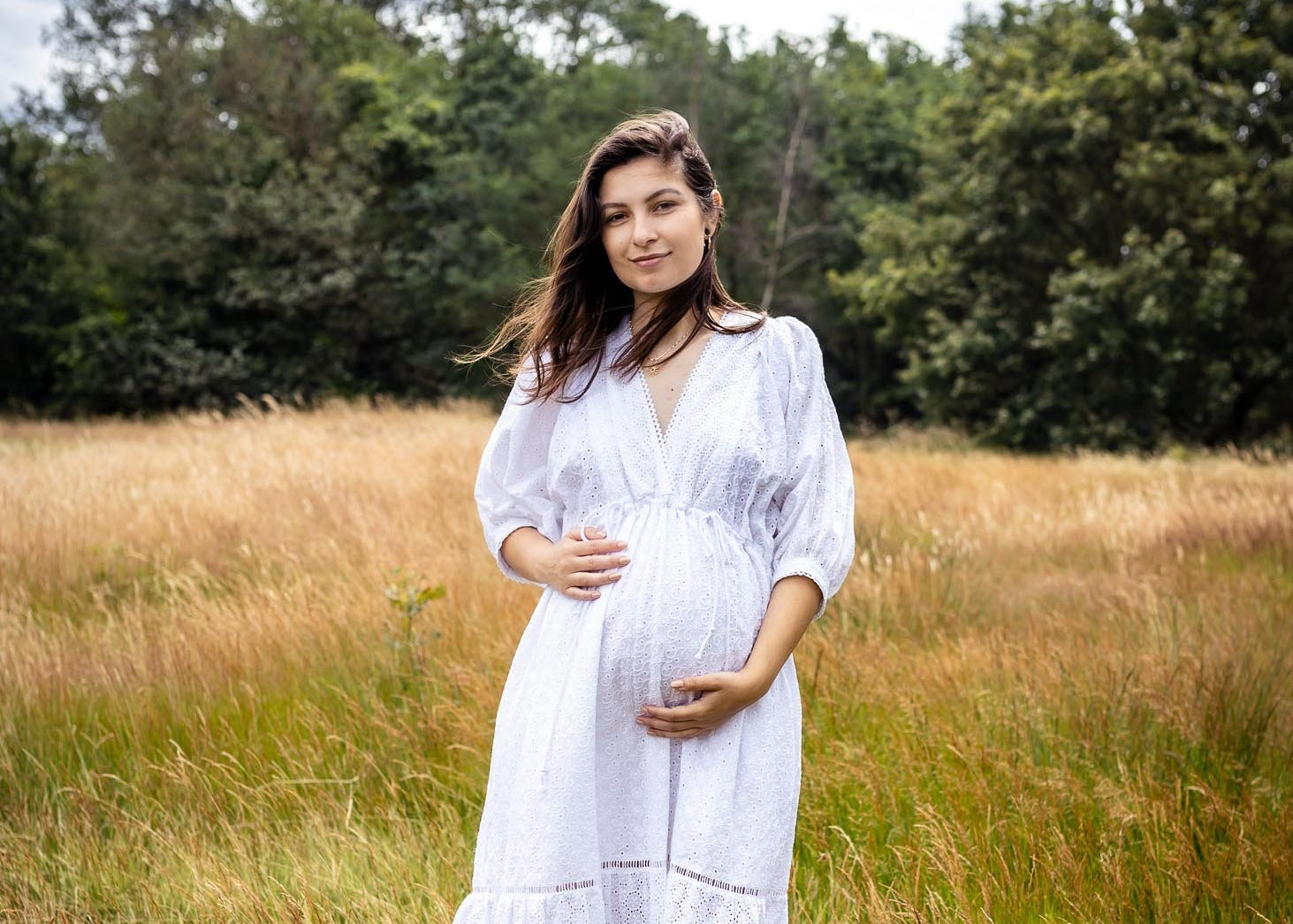 Woman in a white dress standing in a field with trees in the background