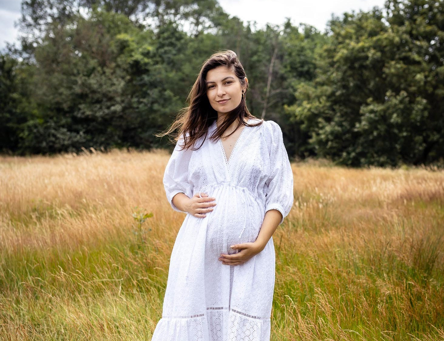 Woman in a white dress standing in a field with trees in the background