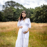 Woman in a white dress standing in a field with trees in the background