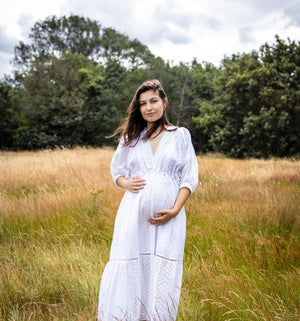 Woman in a white dress standing in a field with trees in the background