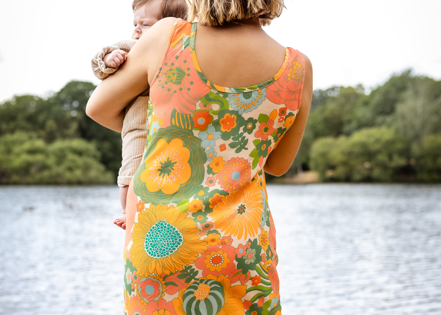 Woman in a floral dress holding a child by a lake
