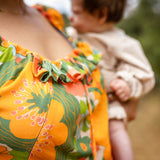 Person wearing a colorful floral dress with a blurred child in the background