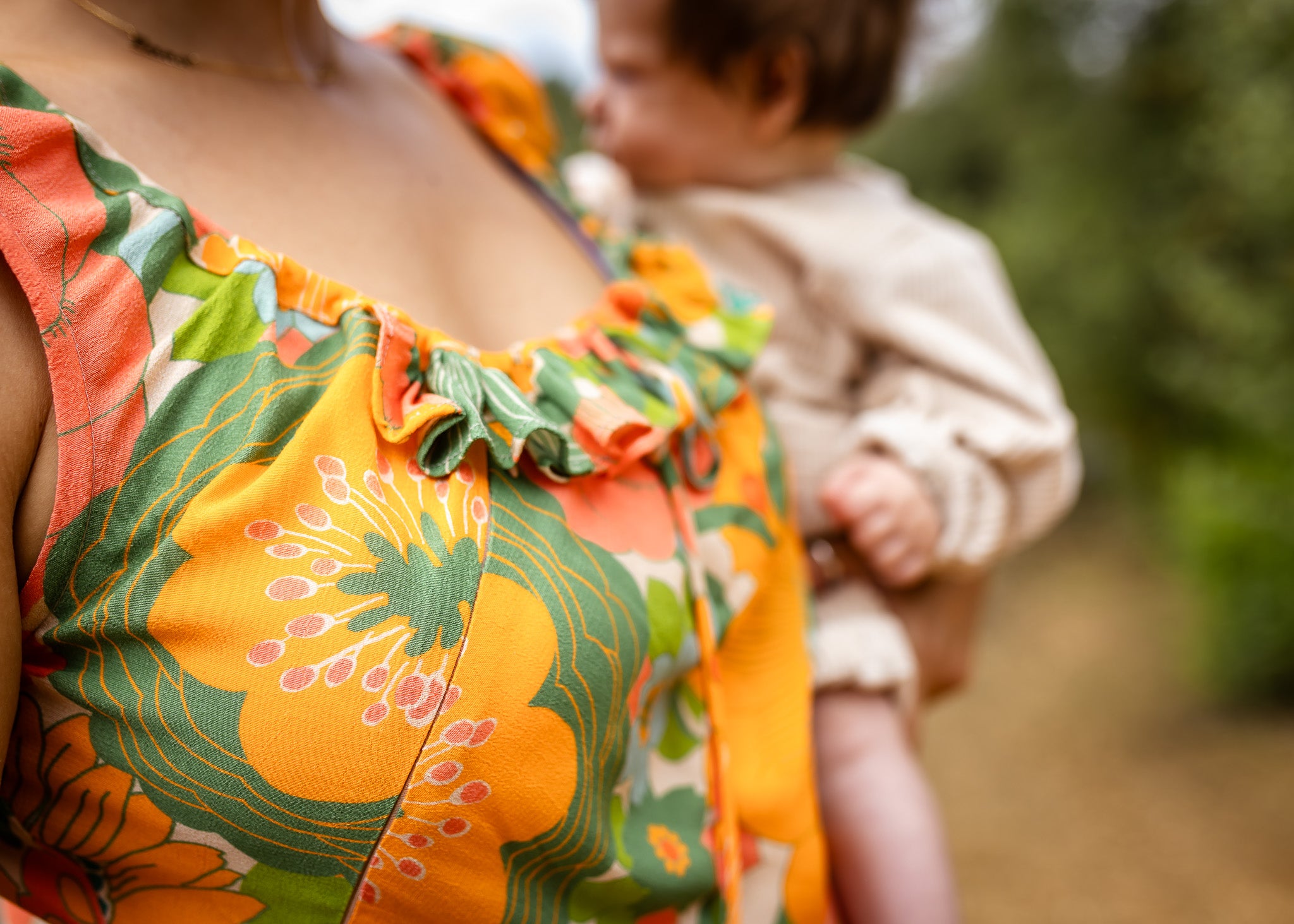 Person wearing a colorful floral dress with a blurred child in the background
