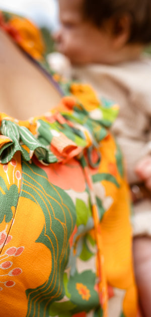 Person wearing a colorful floral dress with a blurred child in the background