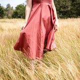 A woman wearing a dusty rose pink midi skirt walks through a field of dry golden grass.