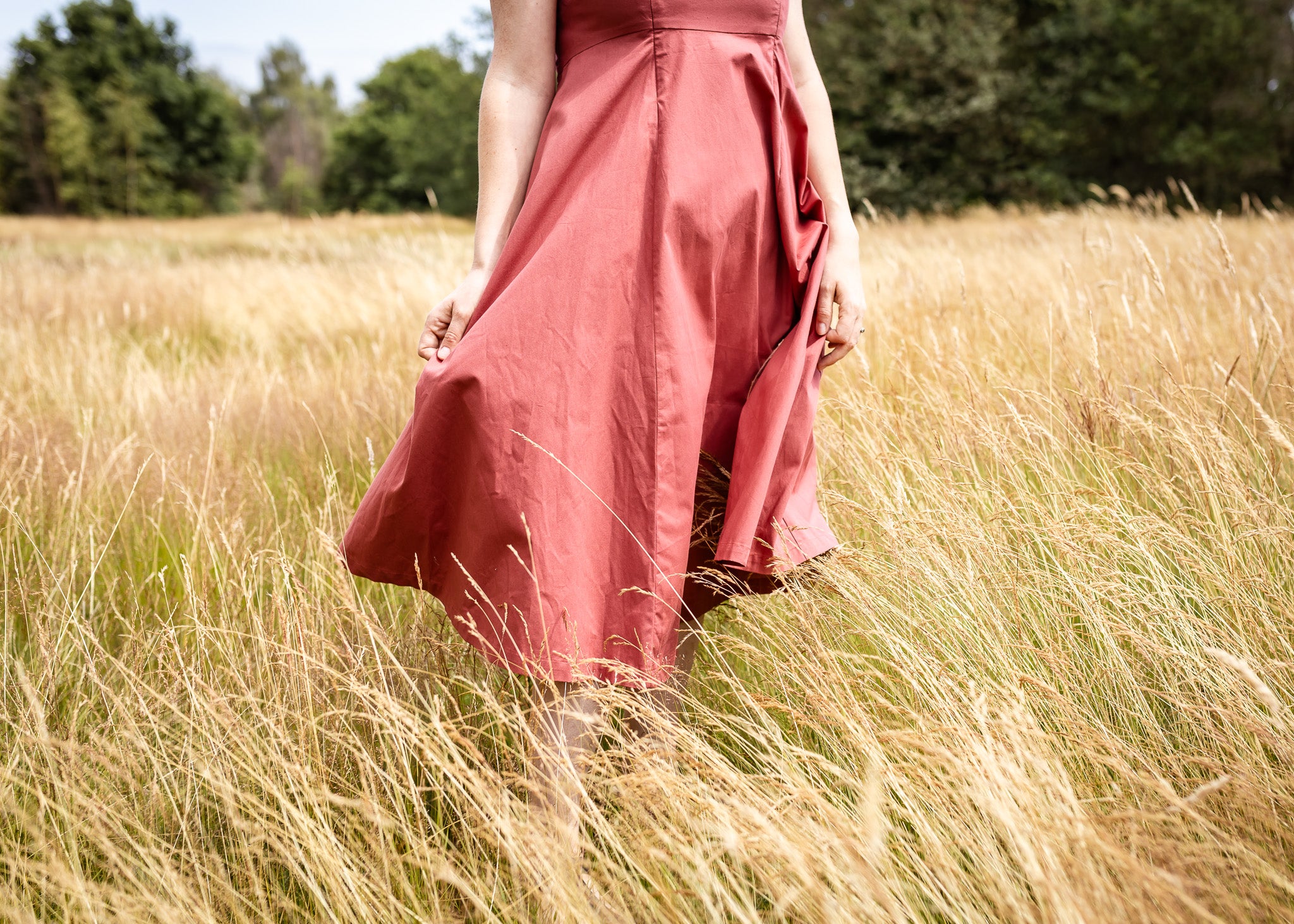 A woman wearing a dusty rose pink midi skirt walks through a field of dry golden grass.