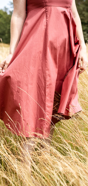 A woman wearing a dusty rose pink midi skirt walks through a field of dry golden grass.