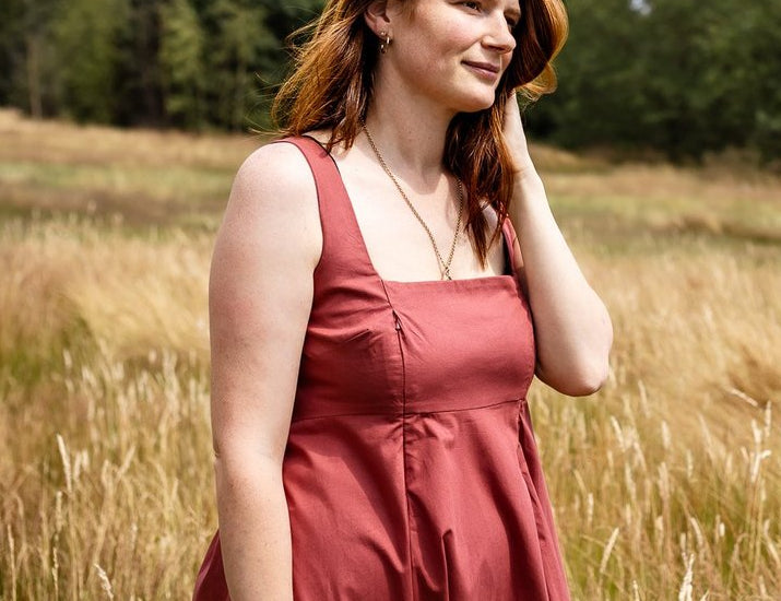 Woman in a red dress standing in a field with trees in the background