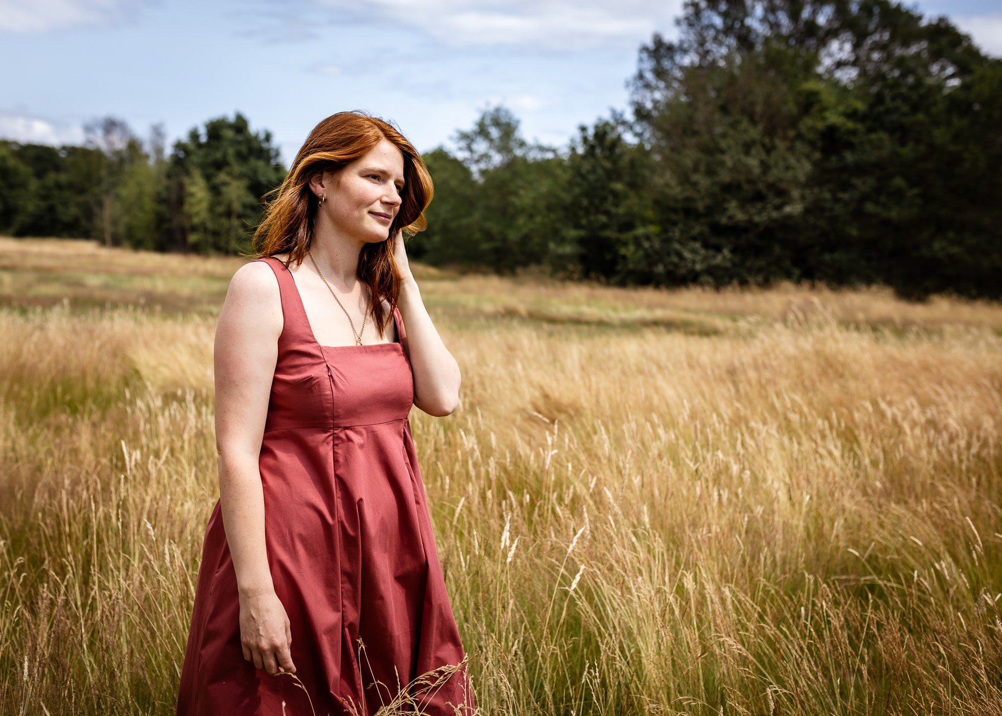 Woman in a red dress standing in a field with trees in the background