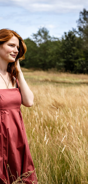 Woman in a red dress standing in a field with trees in the background