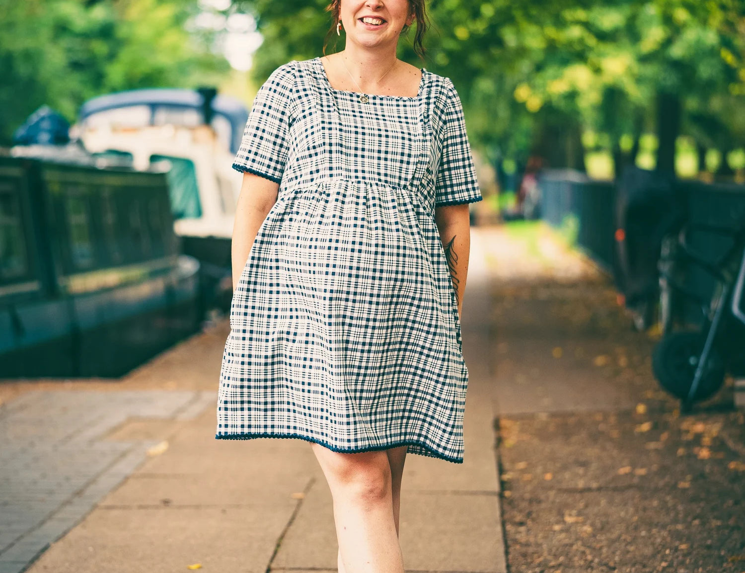 Woman in a checkered dress standing on a sidewalk with greenery in the background