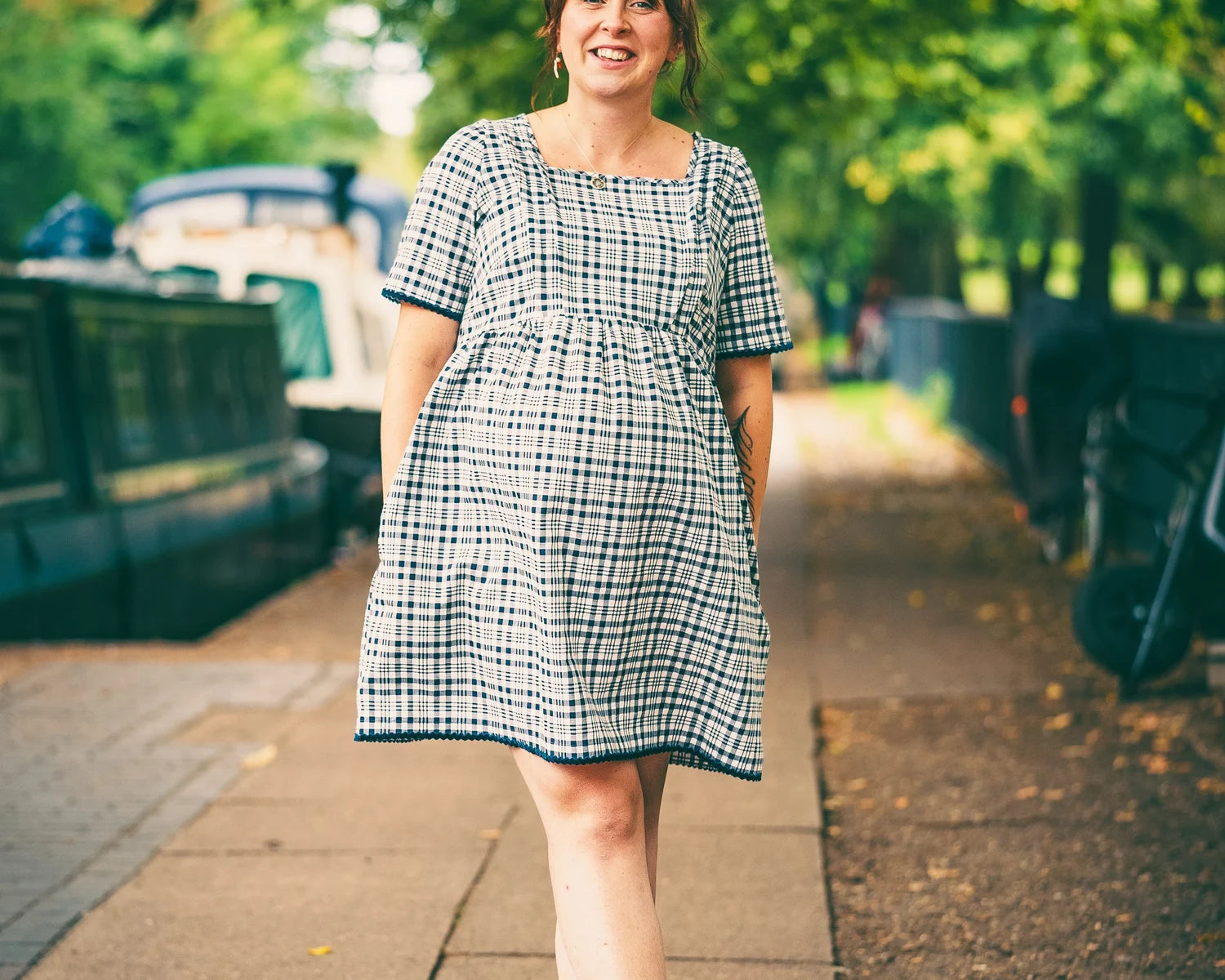 Woman in a checkered dress standing on a sidewalk with greenery in the background