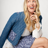 Woman wearing a blue quilted jacket and floral skirt sitting on a white chair.