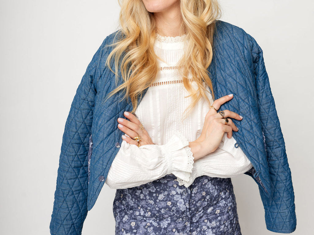 Woman wearing a blue quilted jacket, white blouse, and floral skirt on a plain background