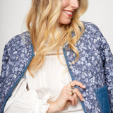 Woman wearing a blue floral jacket over a white top against a plain background