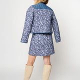 Woman wearing a blue floral jacket and skirt set with beige knee-high boots on a white background