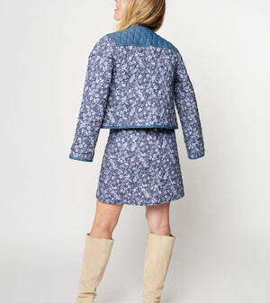 Woman wearing a blue floral jacket and skirt set with beige knee-high boots on a white background