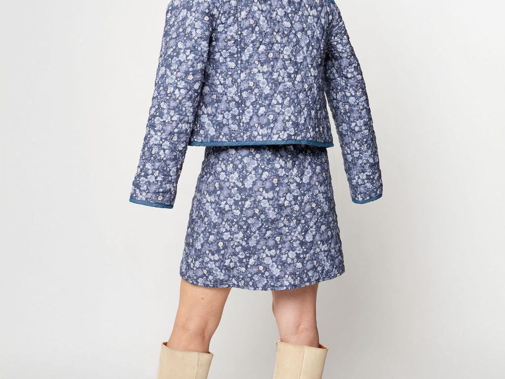 Woman wearing a blue floral jacket and skirt set with beige knee-high boots on a white background