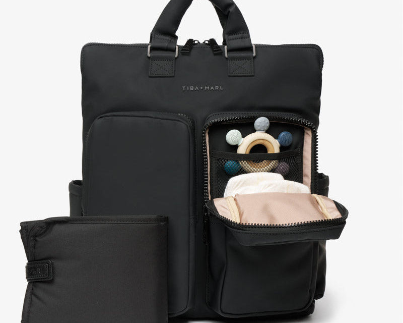 Black backpack with a smaller pouch, open to reveal baby items on a light gray background