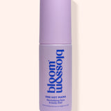 A lavender purple cylindrical bottle of bloom & soho One Hot Mama Revitalising Face & Body Mist, shown against a solid pale peach background.