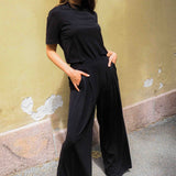 Woman wearing a black outfit standing against a textured wall.