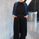 Woman in black outfit with blue cardigan standing against a concrete wall.