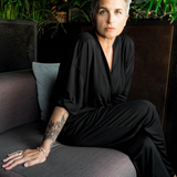 Person in a black outfit sitting on a gray couch with greenery in the background