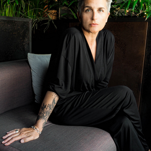 Person in a black outfit sitting on a gray couch with greenery in the background