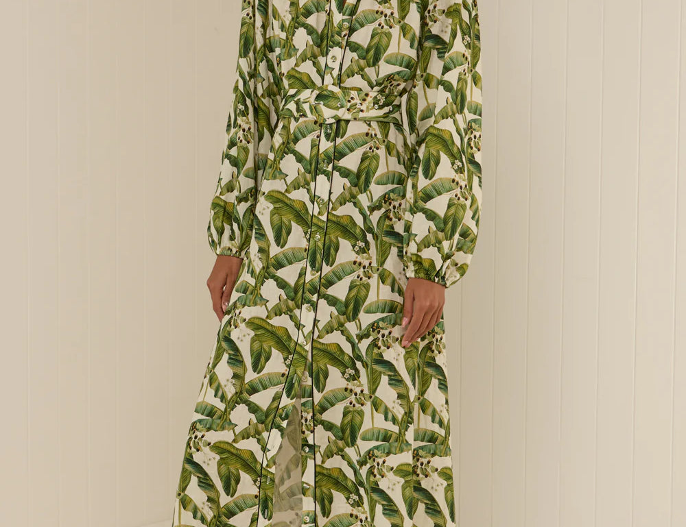 Woman wearing a long green leaf-patterned dress against a white background