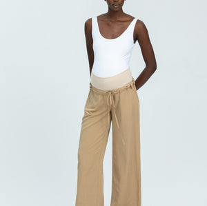 Woman wearing a white tank top and beige wide-leg pants on a white background