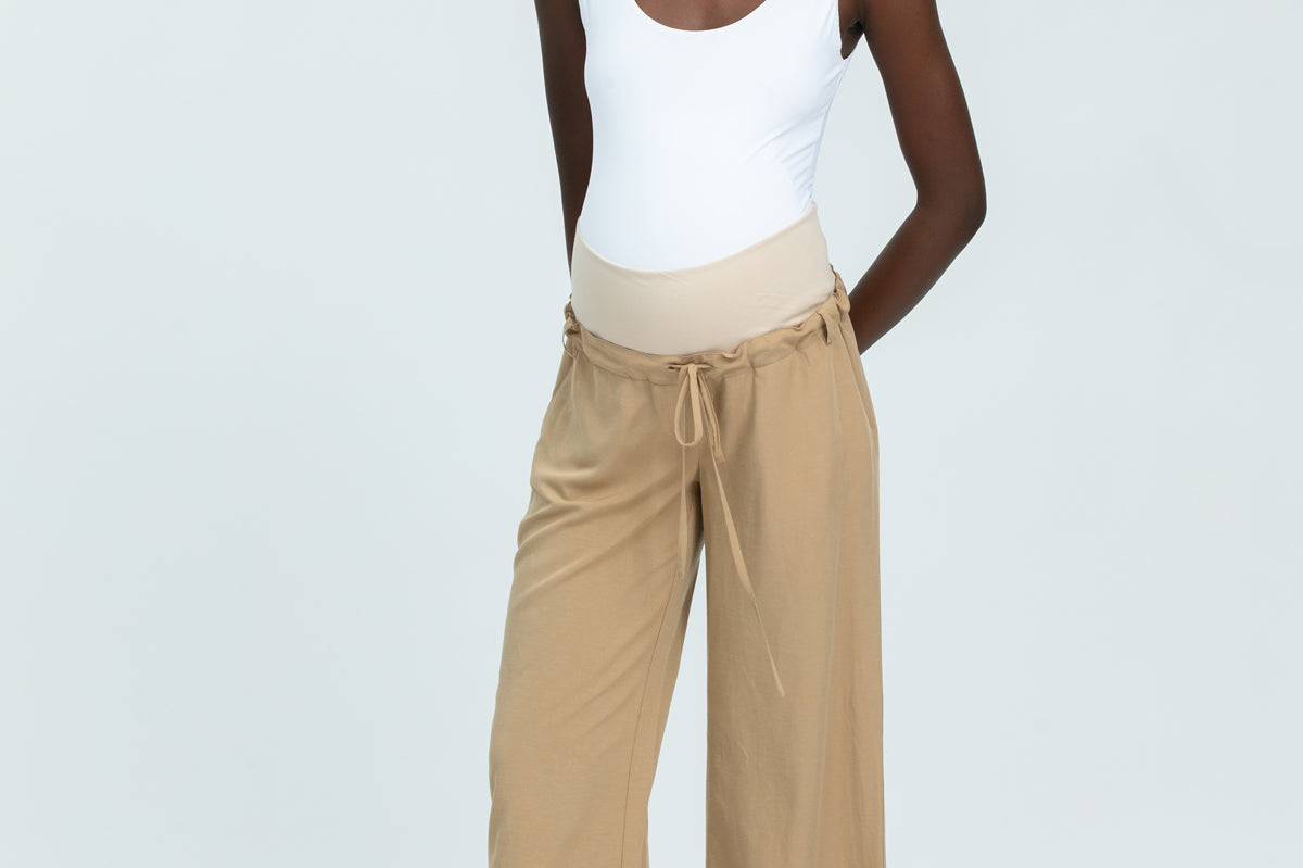Woman wearing a white tank top and beige wide-leg pants on a white background